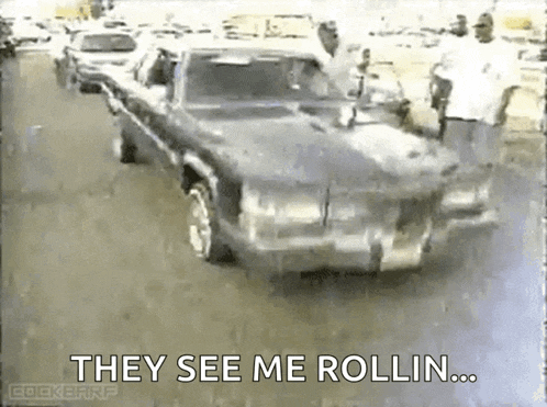 a black car is driving down a street with the words they see me rollin