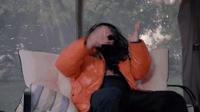 a person wearing an orange jacket and sunglasses is sitting on a couch