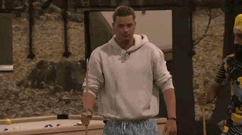a man in a white hoodie is holding a pool cue .