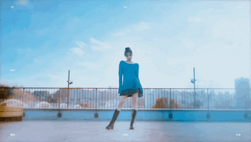 a woman in a blue dress and boots stands on a balcony with the number 87 on the bottom
