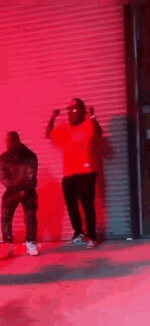two men are dancing in front of a red wall in a dark room .