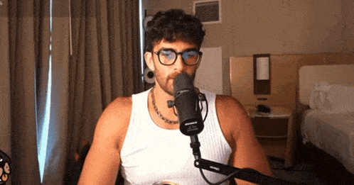 a man wearing glasses and a white tank top is sitting in front of a microphone