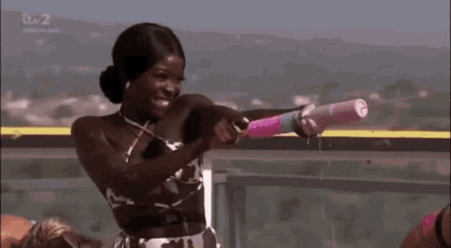 a woman in a bikini is holding a water gun while standing on a balcony .