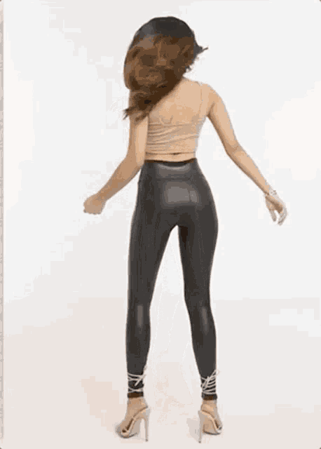 a woman wearing a crop top and leather pants is standing in front of a white background .