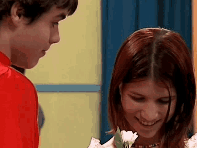 a boy and a girl are looking at each other while the girl is holding a flower .