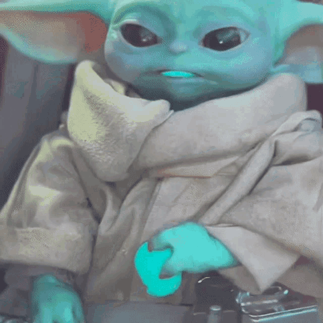 a baby yoda from star wars is holding a blue object in its mouth .
