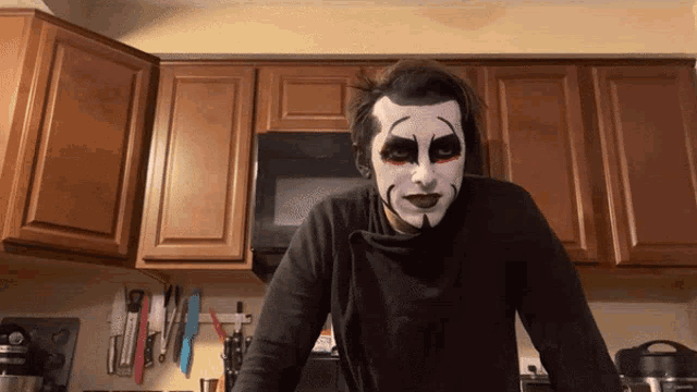 a man in a black shirt with a face painted like kiss is standing in a kitchen