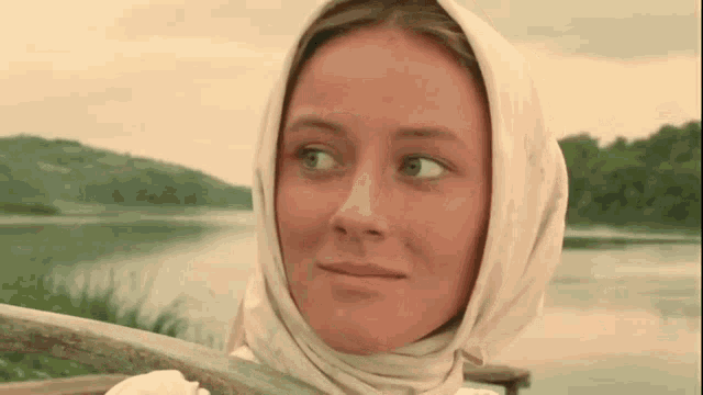 a woman wearing a white scarf around her head is standing in front of a body of water .
