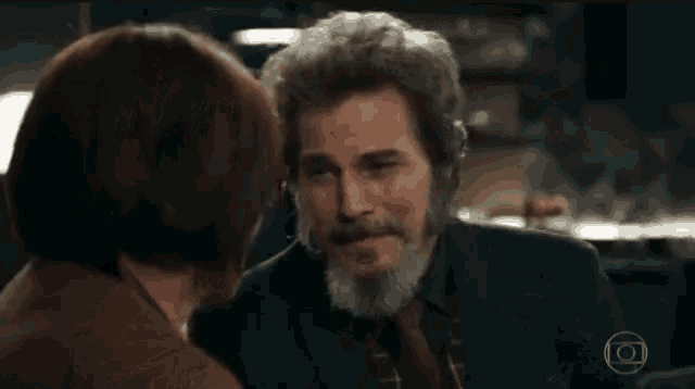 a woman is touching a man 's face with her hand while they are looking at each other .