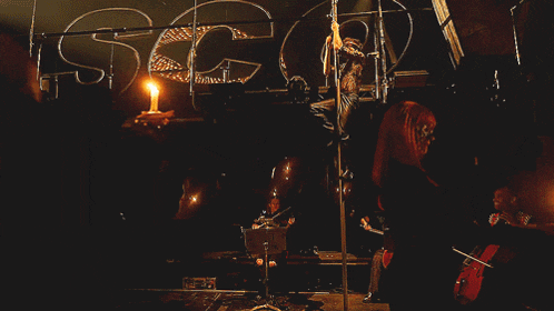 a man is standing on a pole while a woman plays violin in the background