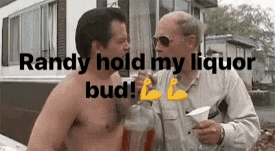 a shirtless man is holding a bottle of liquor and talking to another man .