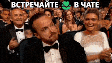 a man in a tuxedo and bow tie is sitting in a crowd of people with the words " встречайте " in green