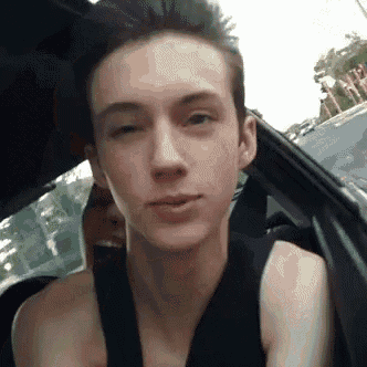 a young man without a shirt is sitting in a car looking at the camera .