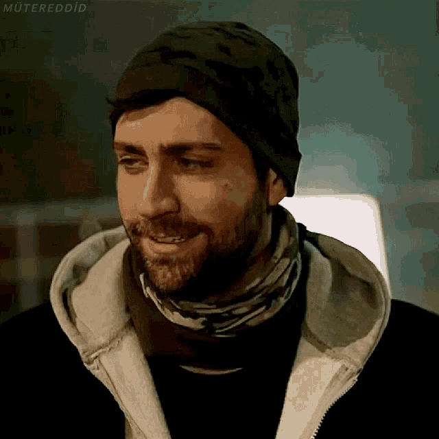 a man with a beard wearing a beanie and scarf smiles for the camera