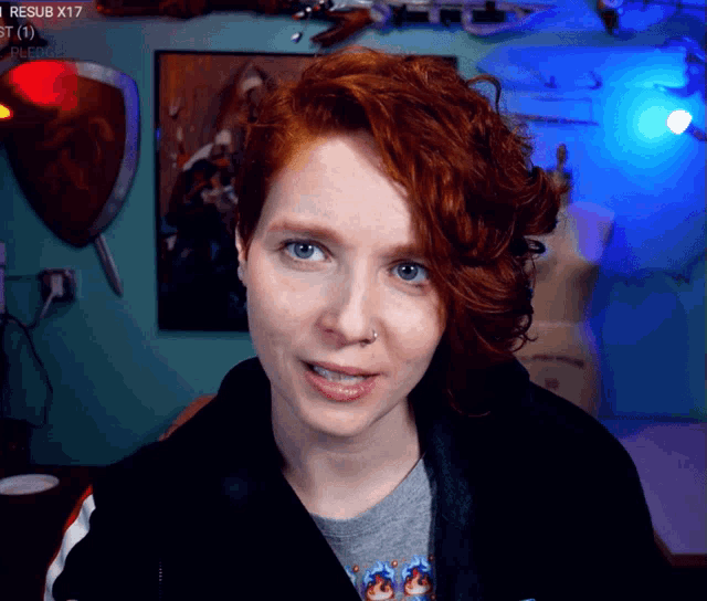 a woman with red hair looks at the camera in front of a sign that says resub x17 on it