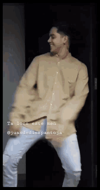 a man in a tan shirt and white jeans is dancing in front of a door .