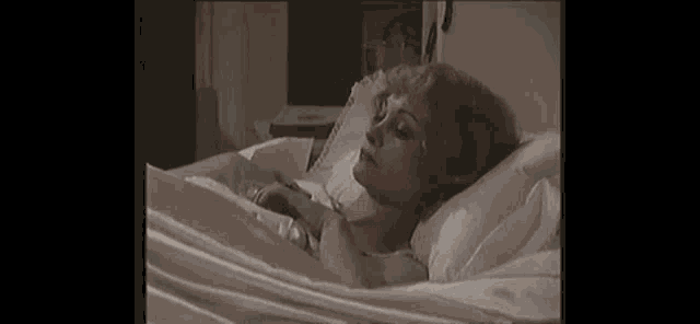 a woman is laying in a bed with white sheets and pillows and looking at the camera .