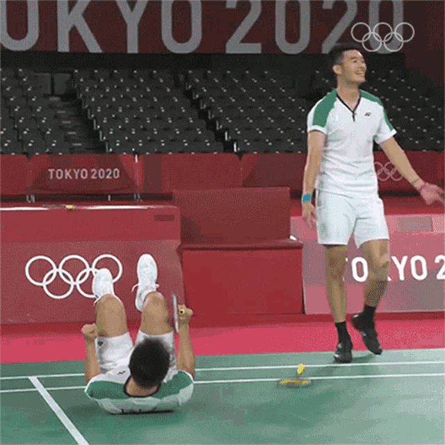 two men are playing badminton in front of a tokyo 2020 banner
