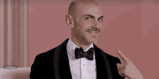 a man in a tuxedo and bow tie points to a sign that says will nana