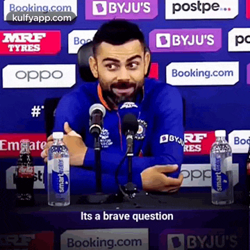 a man in a blue shirt is sitting in front of a microphone and talking .