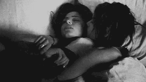 a black and white photo of a man and a woman hugging each other in bed .