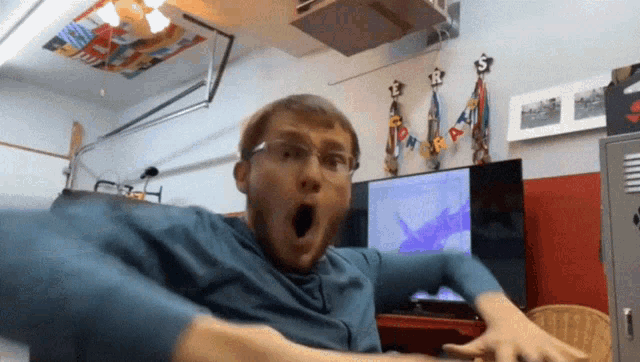 a man in a blue shirt is making a funny face in front of a tv screen that says ' a '