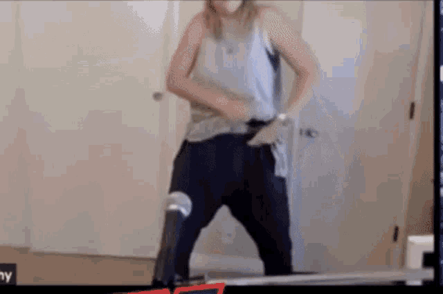 a woman in a tank top and black pants is standing in front of a mirror .