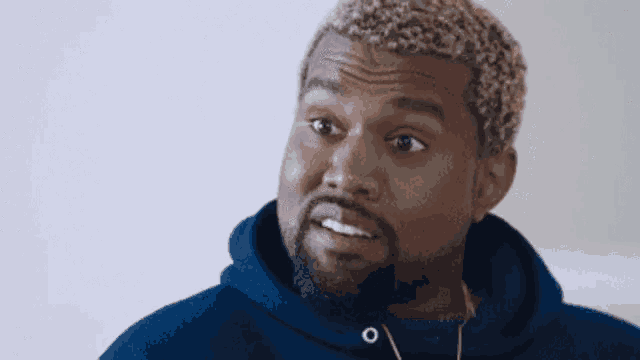 kanye west is wearing a blue hoodie and headphones while making a funny face .