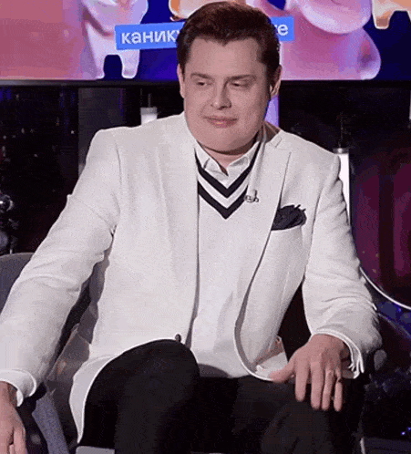 a man in a white suit is sitting in front of a screen that says " kanik "