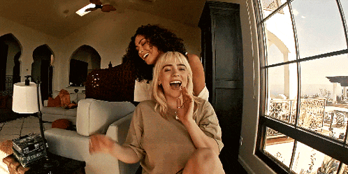 two women are laughing in front of a window and one of them has a book on the table that says polaroid