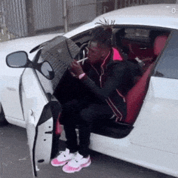 a man with dreadlocks is sitting in the back seat of a white car smoking a cigarette .