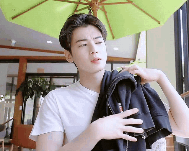 a young man wearing a white t-shirt is holding a black jacket over his shoulder .