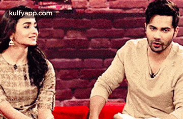 a man and a woman are sitting next to each other on a couch in front of a brick wall .