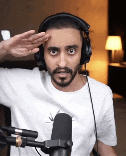 a man with a beard wearing headphones salutes in front of a microphone