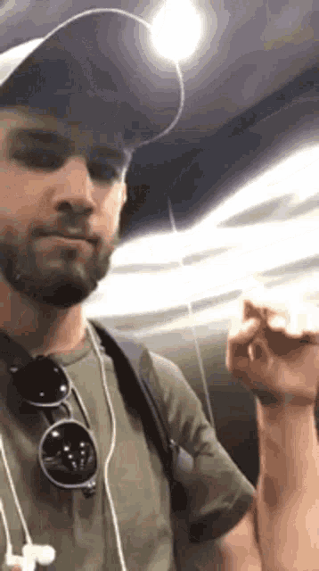 a man wearing a hat and sunglasses is standing in an elevator and flexing his muscles .