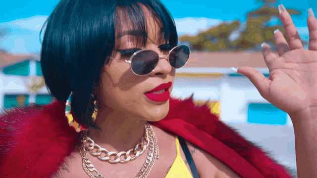 a woman wearing sunglasses and a red fur coat waves her hand