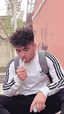 a man smoking a cigarette wearing a white adidas shirt