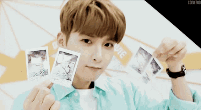 a young man in a blue shirt holds up two polaroid pictures with the word movie in the background