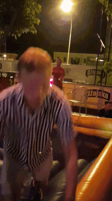 a man in a striped shirt is standing in front of a sign that says ' uzujsko '