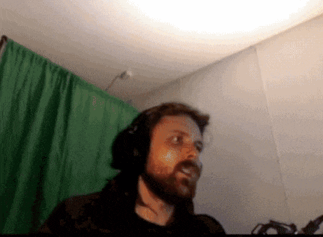 a man with a beard wearing headphones stands in front of a green curtain