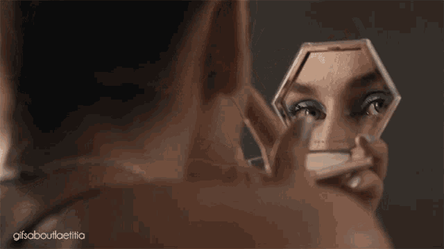 a woman is applying makeup in front of a mirror and the words gifs about ellia are on the bottom