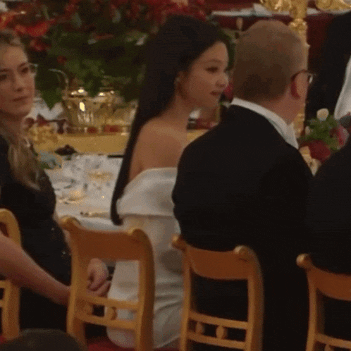 a woman in a white dress is sitting in a wooden chair next to a man in a suit .