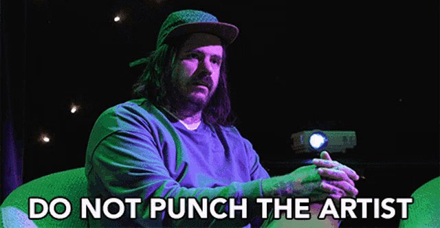 a man sitting in front of a projector with the words do not punch the artist