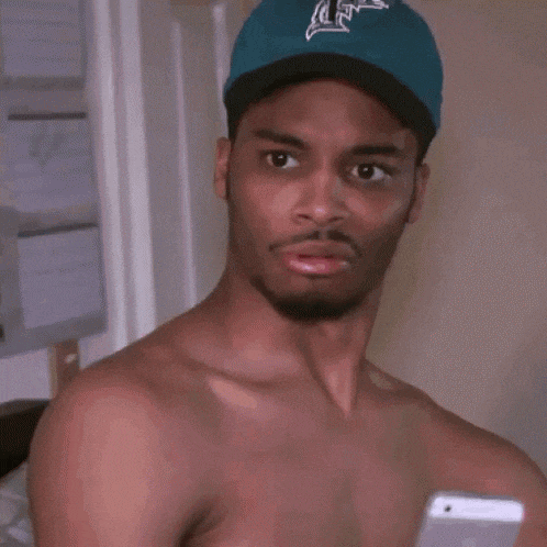 a man without a shirt is wearing a blue hat and making a face .