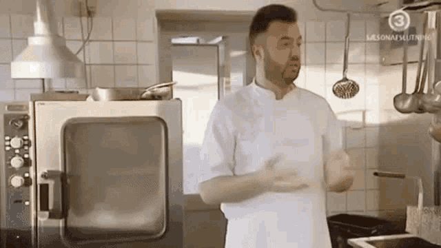 a man in a white chef 's uniform is standing in a kitchen with a large oven .