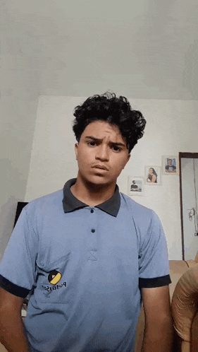 a young man wearing a blue polo shirt with a yellow circle on the pocket making a funny face