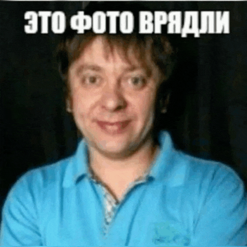 a man in a blue shirt is smiling with his arms crossed in front of a black background with russian writing on it .