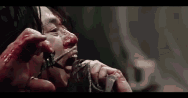 a woman with blood on her face is cutting her hair with scissors .