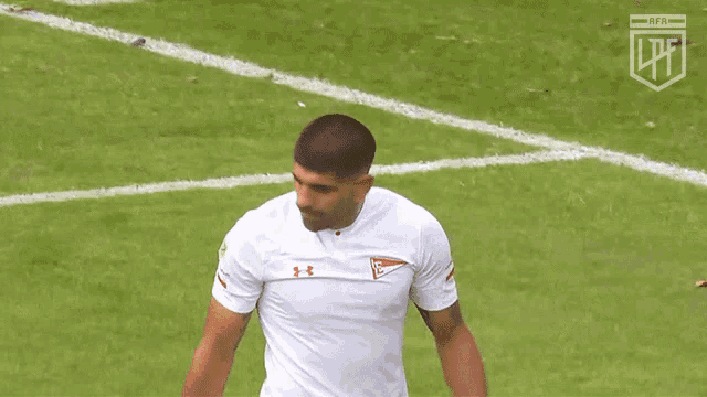 a man in a white under armour shirt stands on a field