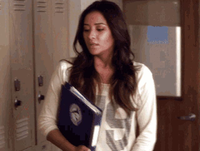 a woman standing in front of a row of lockers holding a blue book